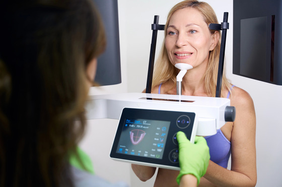 Technology 7 Smiling woman positioned in a cone beam 3D imaging (CBCT) scanner while a dental team member operates the touchscreen.