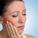 Woman holding her jaw in pain with a red highlight on her cheek, illustrating a toothache that may require a root canal treatment.