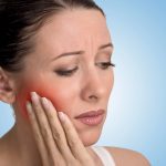 Woman holding her jaw in pain with a red highlight on her cheek, illustrating a toothache that may require a root canal treatment.